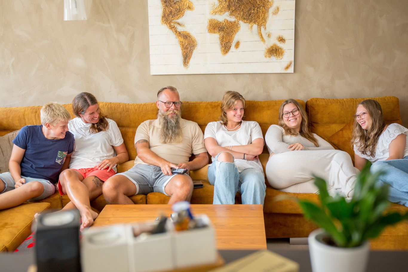 Familj på sex personer sitter tillsammans i en soffa.