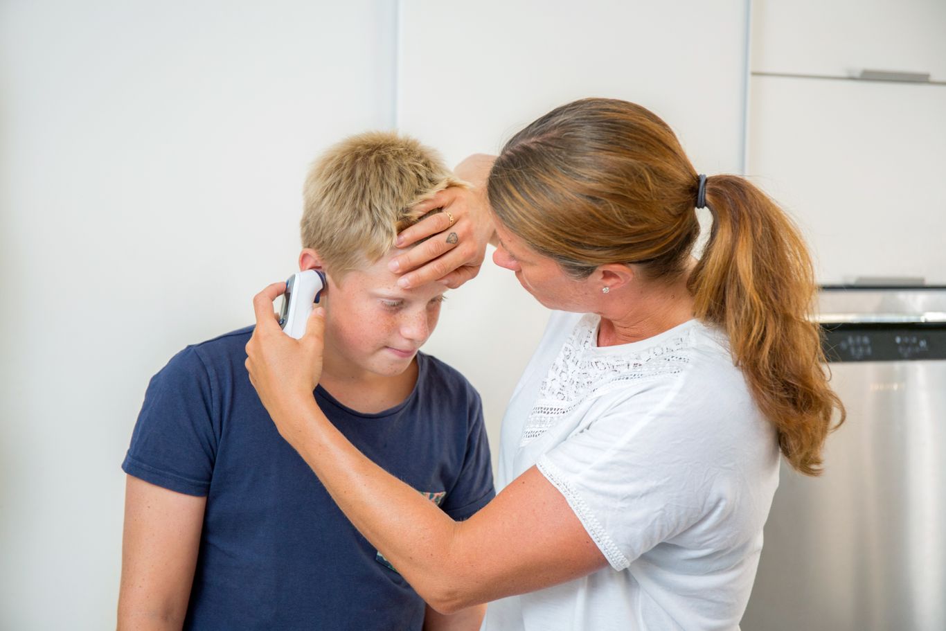 Kvinna mäter feber i örat på ett barn.