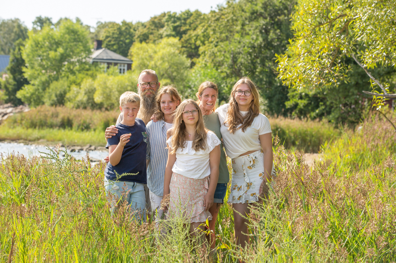 Familj på sex personer poserar tillsammans utomhus.