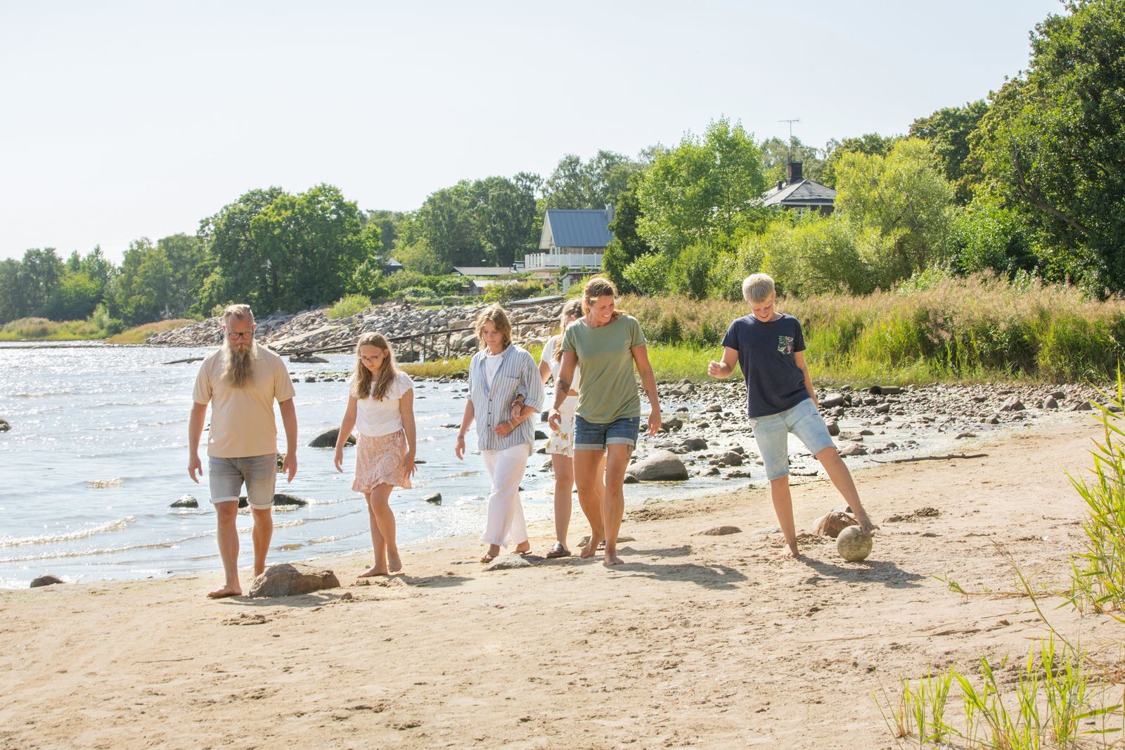 Familj på sex personer promenerar på stranden.
